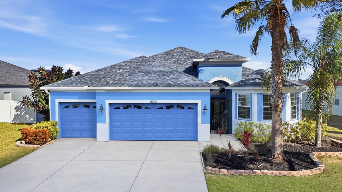 Modern single-story home with bright blue garage doors, white walls, and palm trees in front yard