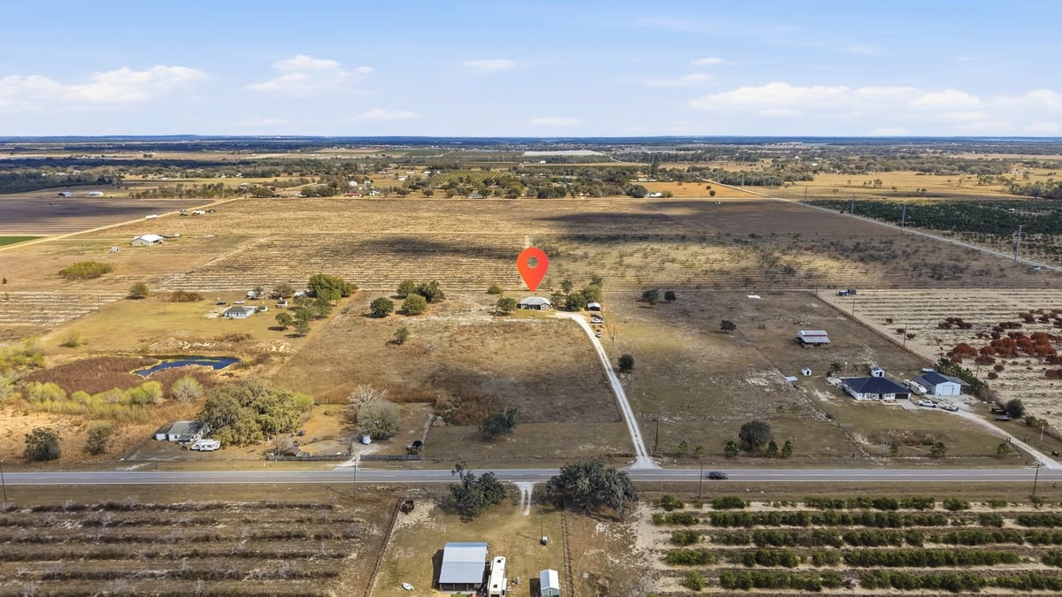 Aerial view of rural farmland with a red pin marker indicating a property location among fields and scattered buildings