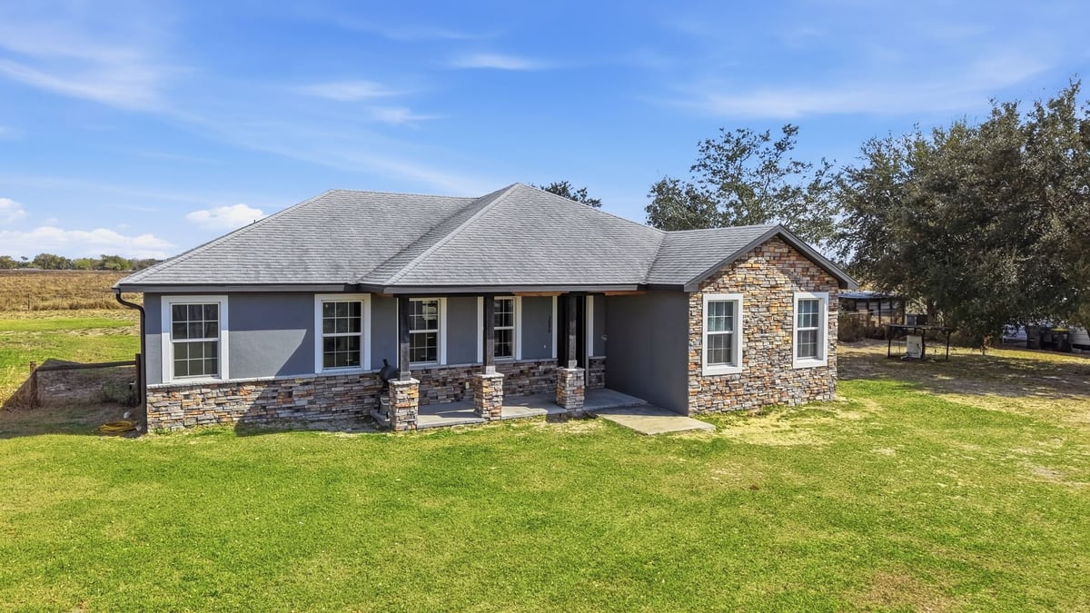 Modern single-story house with stone and dark blue exterior on green lawn with blue sky